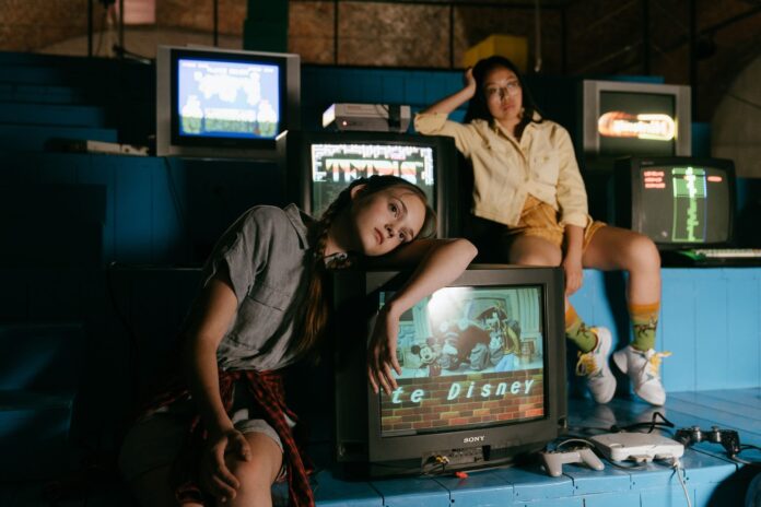 Dwie kobiety grające na retro konsolach przy starych telewizorach Dwie kobiety grające na retro konsolach przy starych telewizorach