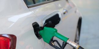 Zielony dystrybutor tankujący białego Volkswagena na stacji paliw